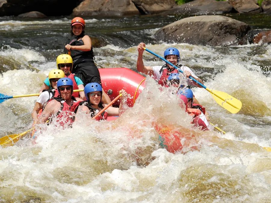 A guide and paddlers navigating whitewater in a red North Creek raft